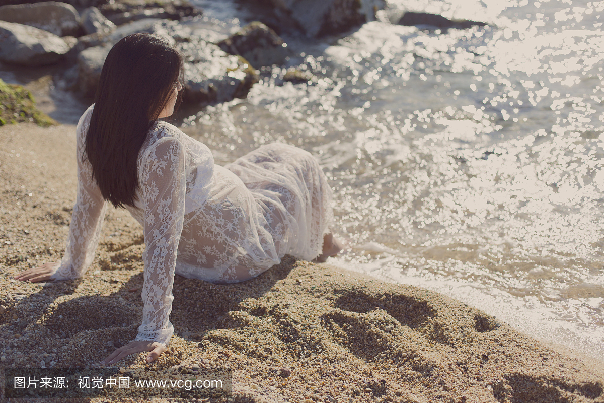 坐在沙滩上的蕾丝礼服的孕妇
