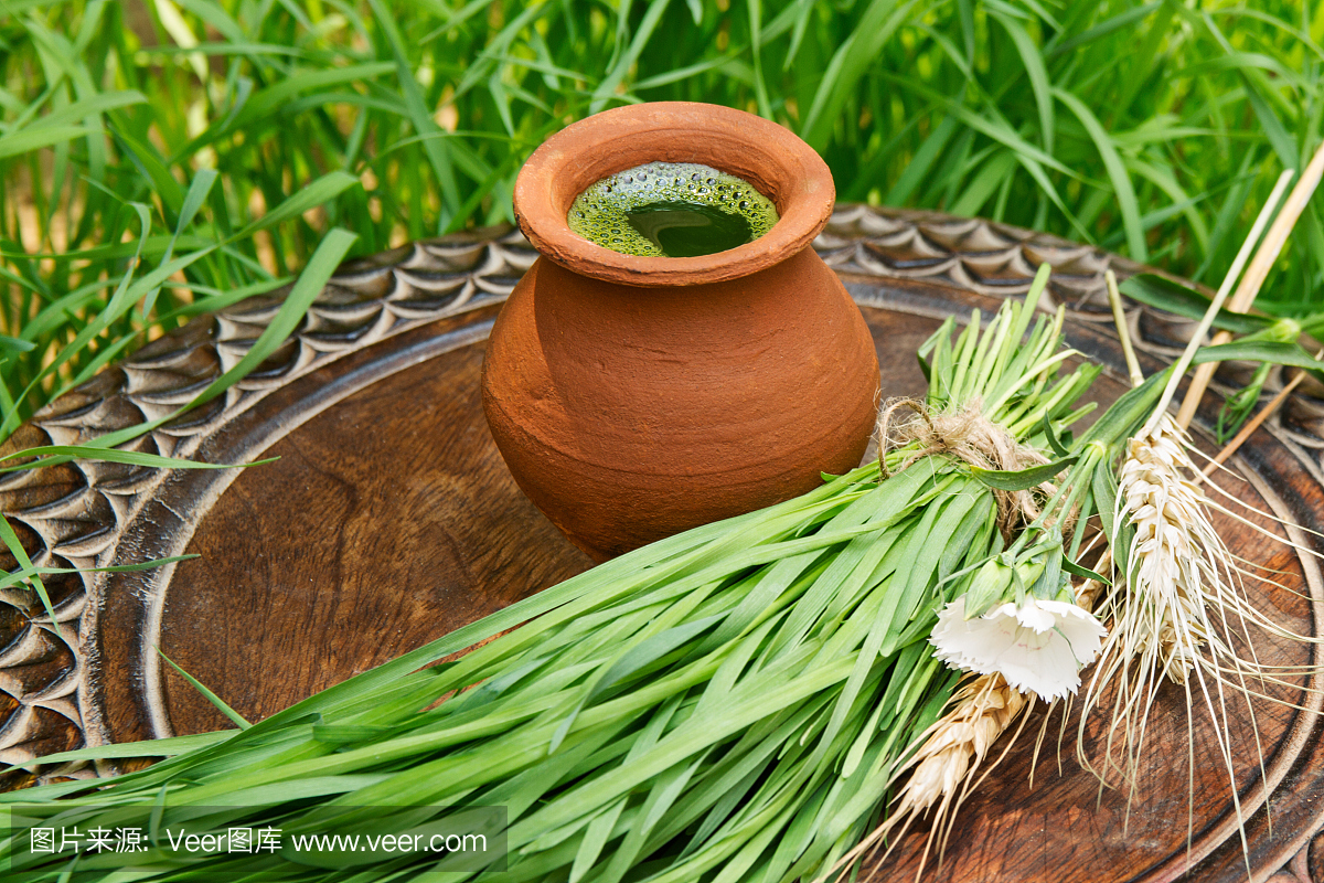 在一个棕色的木桌上的一个陶壶的小麦草汁