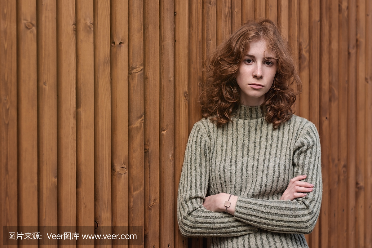 绿色的毛衣上的一个漂亮的红发女孩正站在木墙