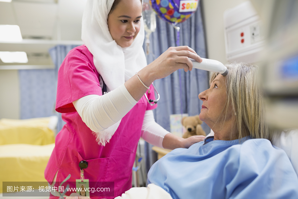 护士戴头盖帽使用额头温度计在病人身上