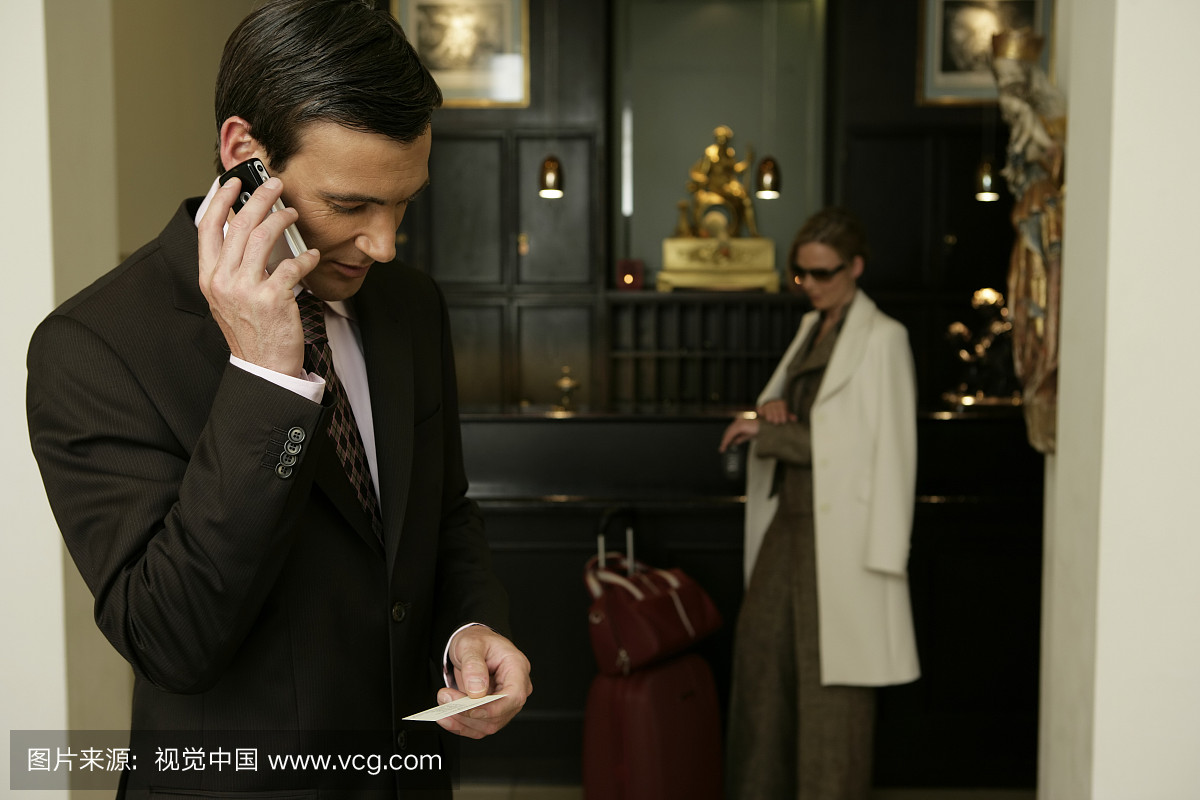 中间的成年夫妇在酒店大堂,男人使用手机,而女
