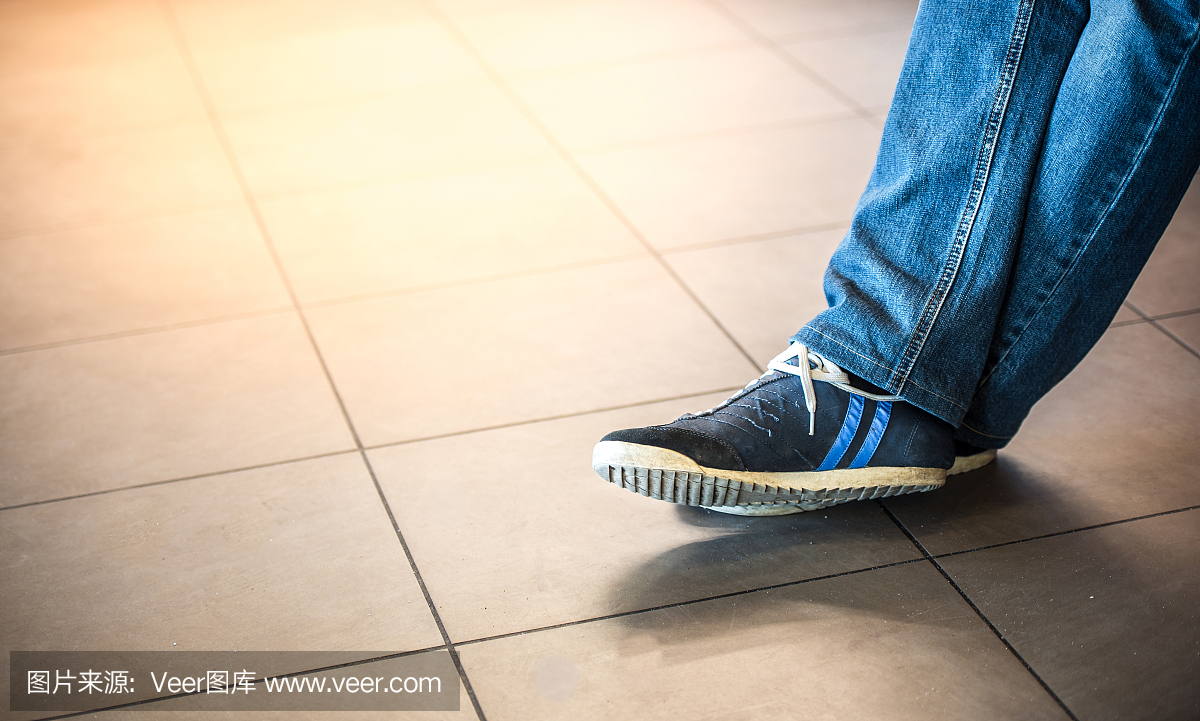 一个人的脚在一个瓷砖地板上的运动鞋。