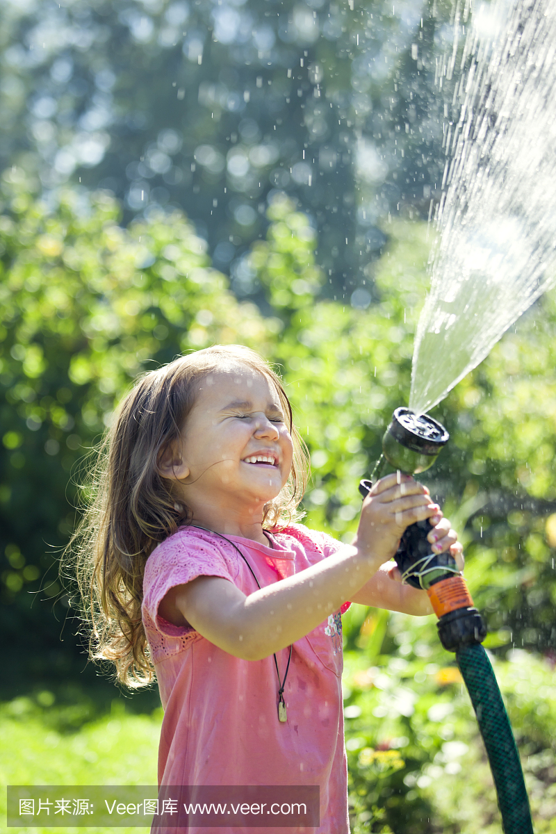 可爱的小女孩在花园里喷洒自己的水