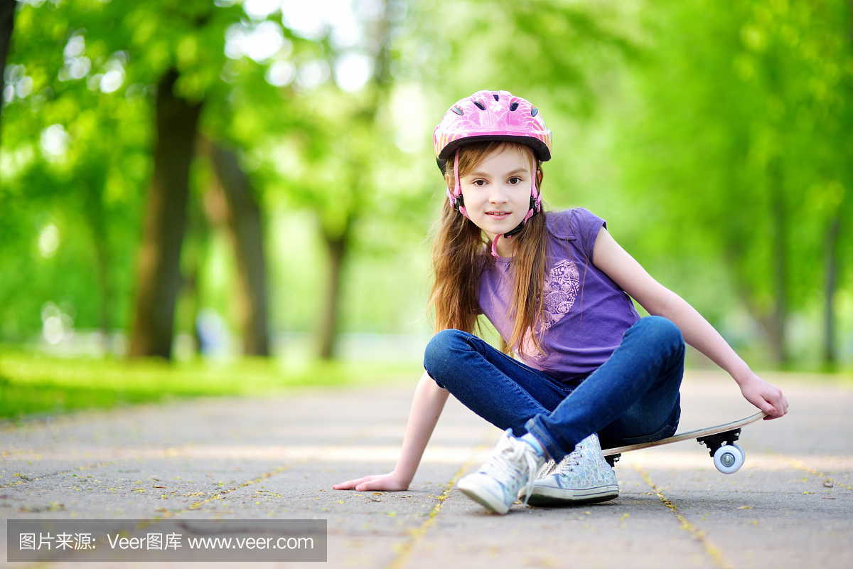 可爱的小青春期前女孩戴着头盔坐在滑板上