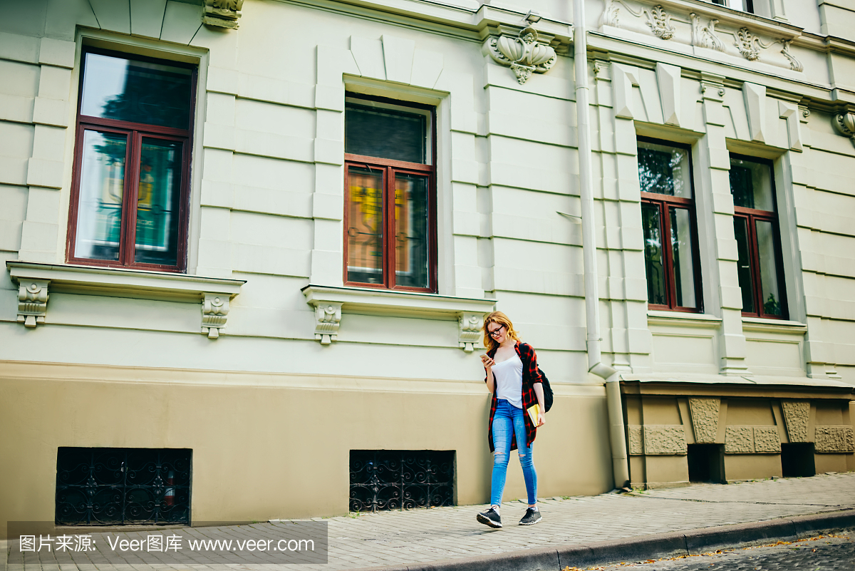 年轻的时髦女孩走在街道上通过建筑物建筑物在