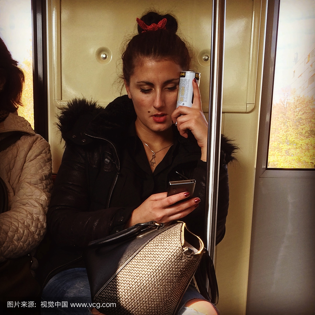 使用移动电话和持有饮料的年轻女子可以在地铁