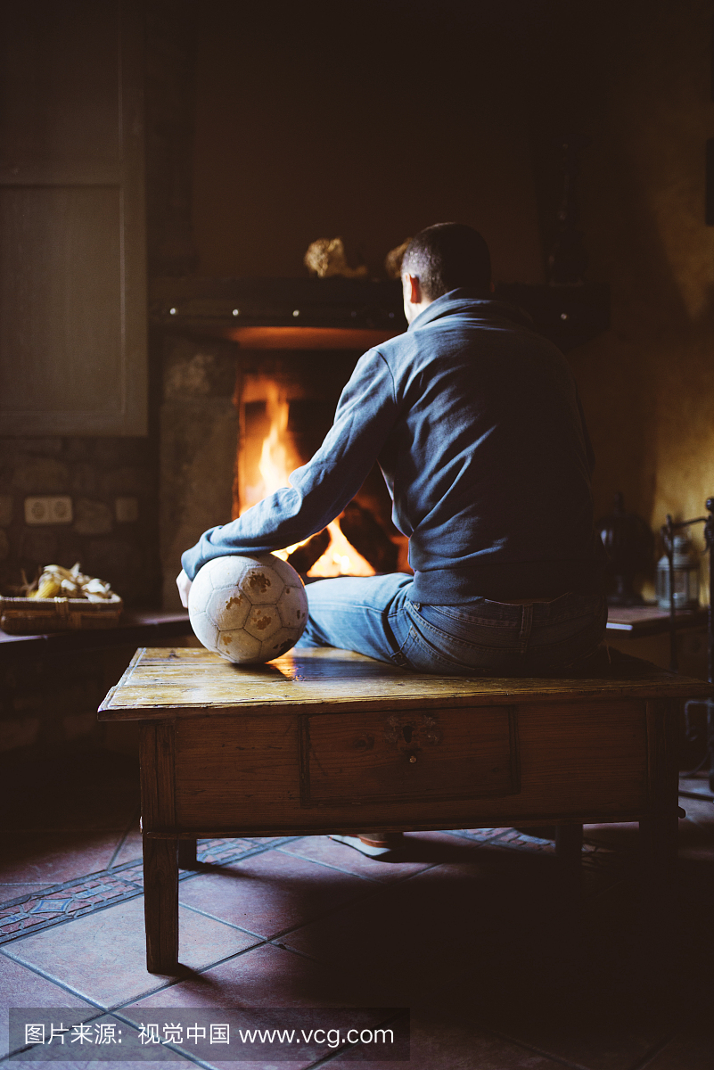 男子坐在壁炉前与一个足球