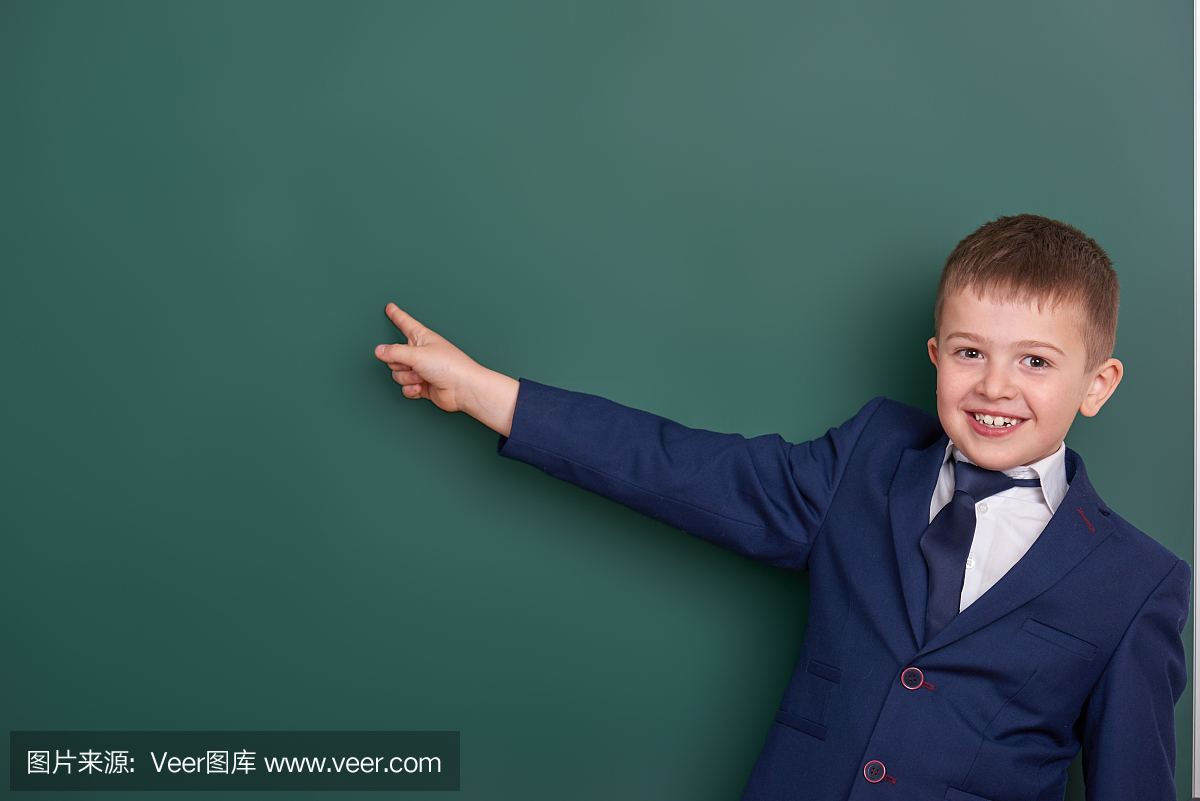 学校男孩指着手指靠近空白的黑板背景,穿着经