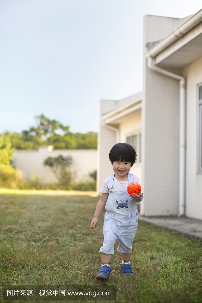 亚洲小孩2到3岁男孩在花园里踢球。