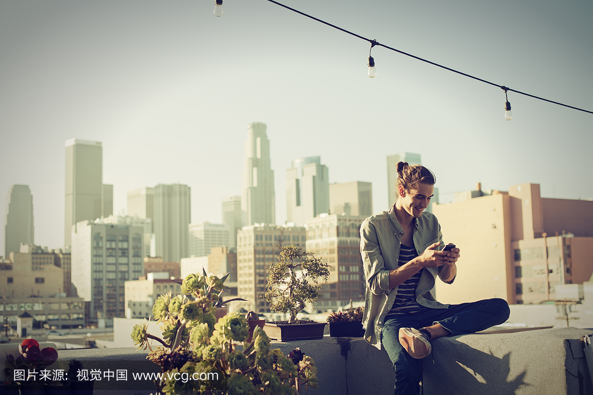 年轻人在城市屋顶上检查他的智能手机