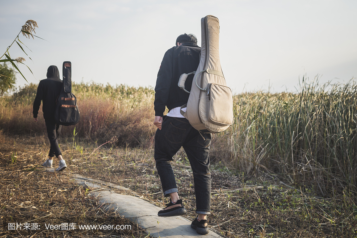 两个男人,朋友走在田野里用吉他