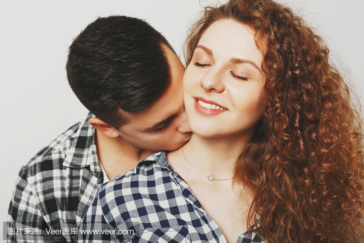 高兴的女性保持闭着眼睛，从她的男友接受脖子上的激情吻。年轻人吻他年轻的妻子，去爱情。恋爱中的夫妻感情很好，很浪漫