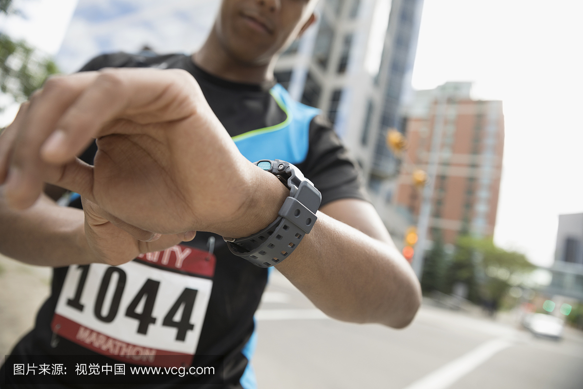 检查在城市街道上的智能手表的男性马拉松运动
