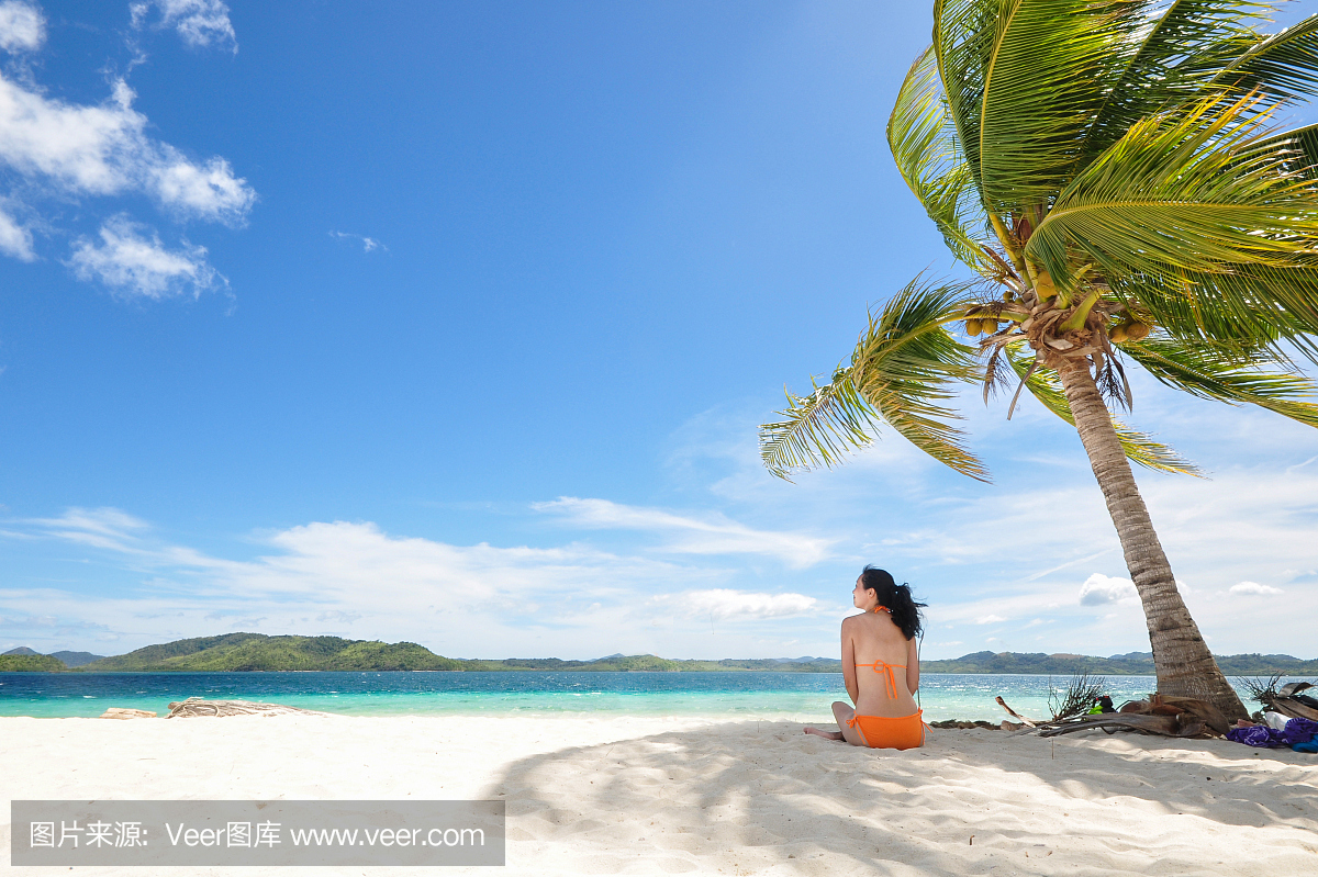 坐在椰子树下的海滩上的年轻女孩