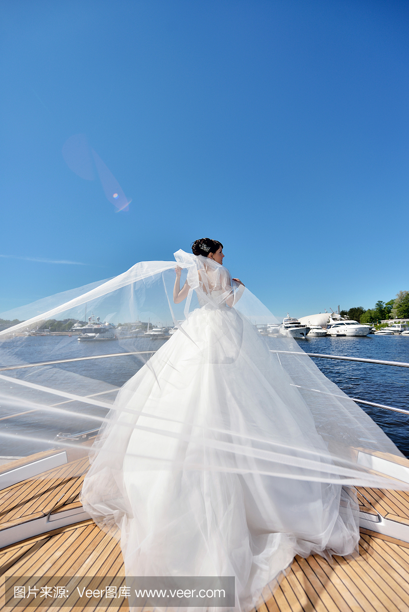 美丽的新娘在婚纱礼服与花边面纱在游艇上