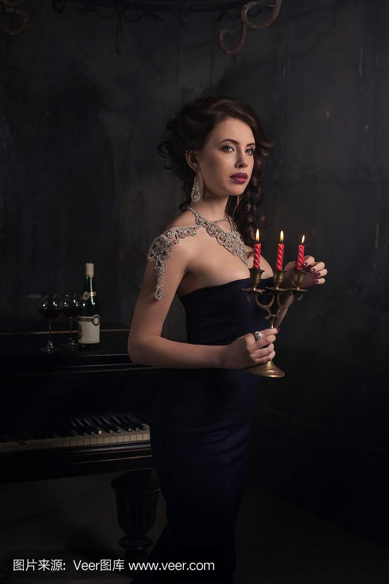 美丽的年轻女子在黑色礼服旁边一个钢琴与烛光
