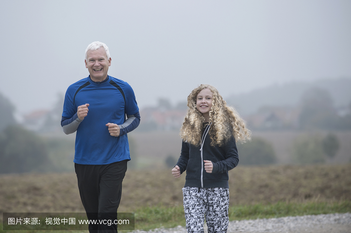 父亲和他的女儿在小径上跑步,黎明时微笑,德国