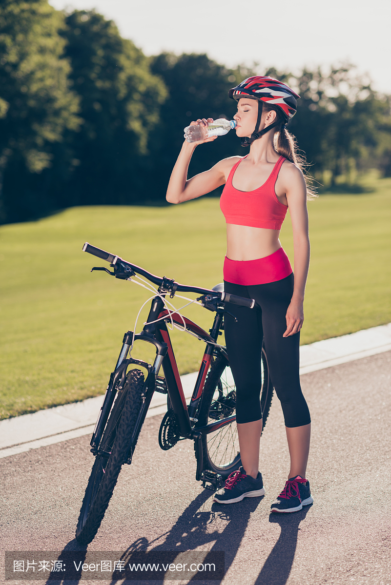 年轻的运动员正在喝水来刷新。她在夏日外面骑