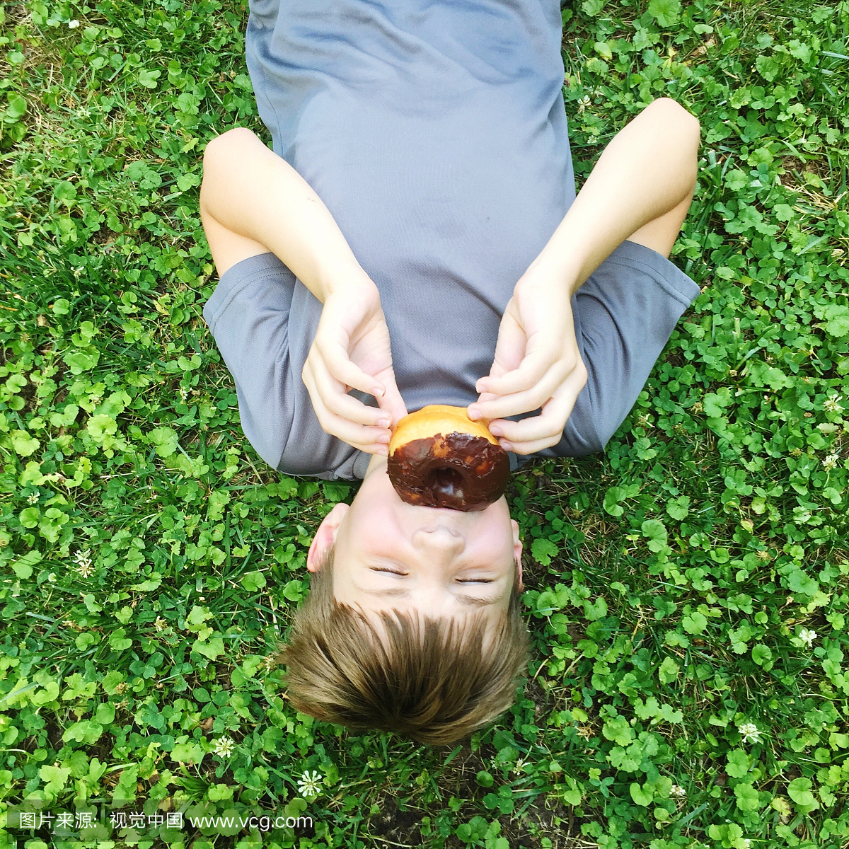 高角度视图的男孩吃甜甜圈,同时躺在公园