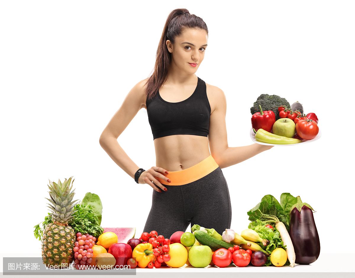 一张桌子后面的健身女孩拿着一盘水果和蔬菜