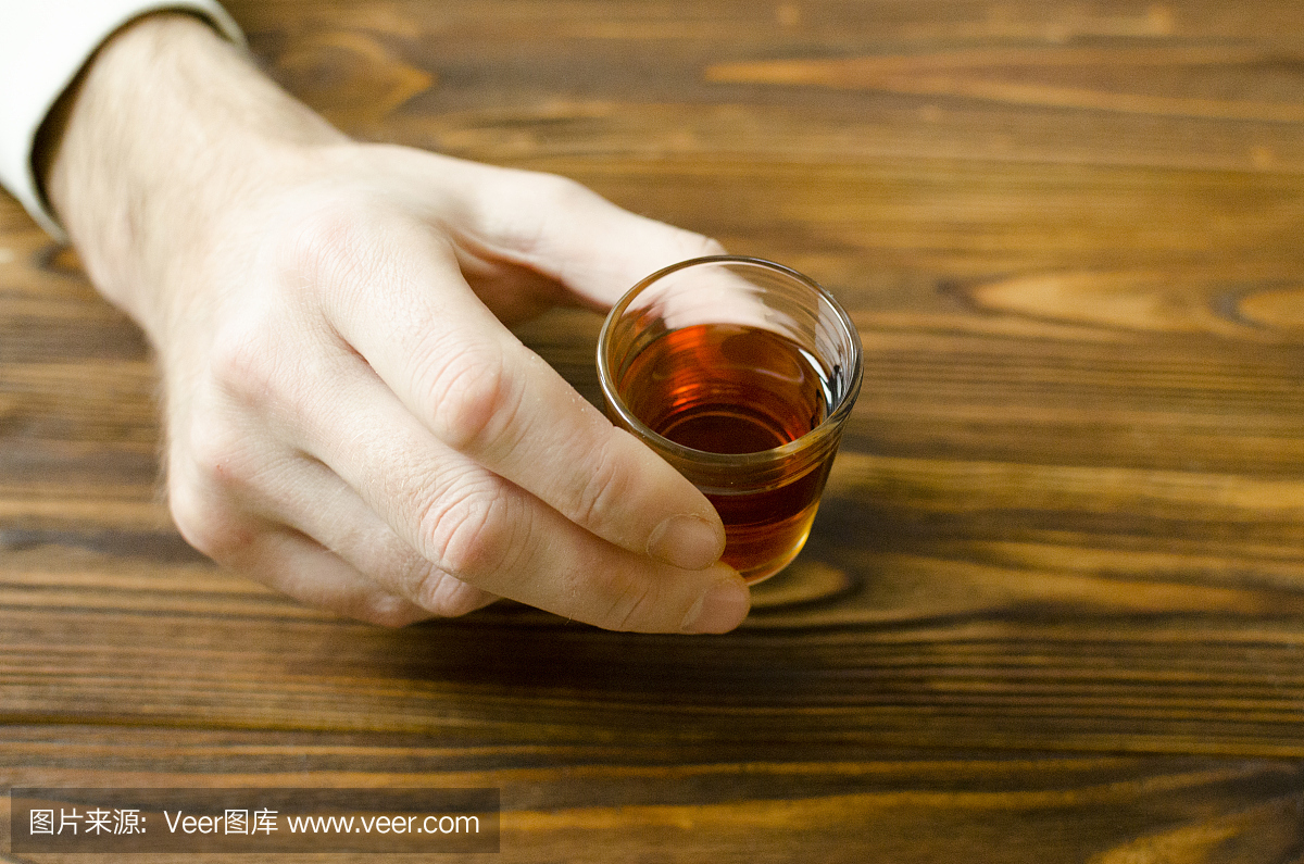 手拿着小酒杯与酒精饮料在木桌上