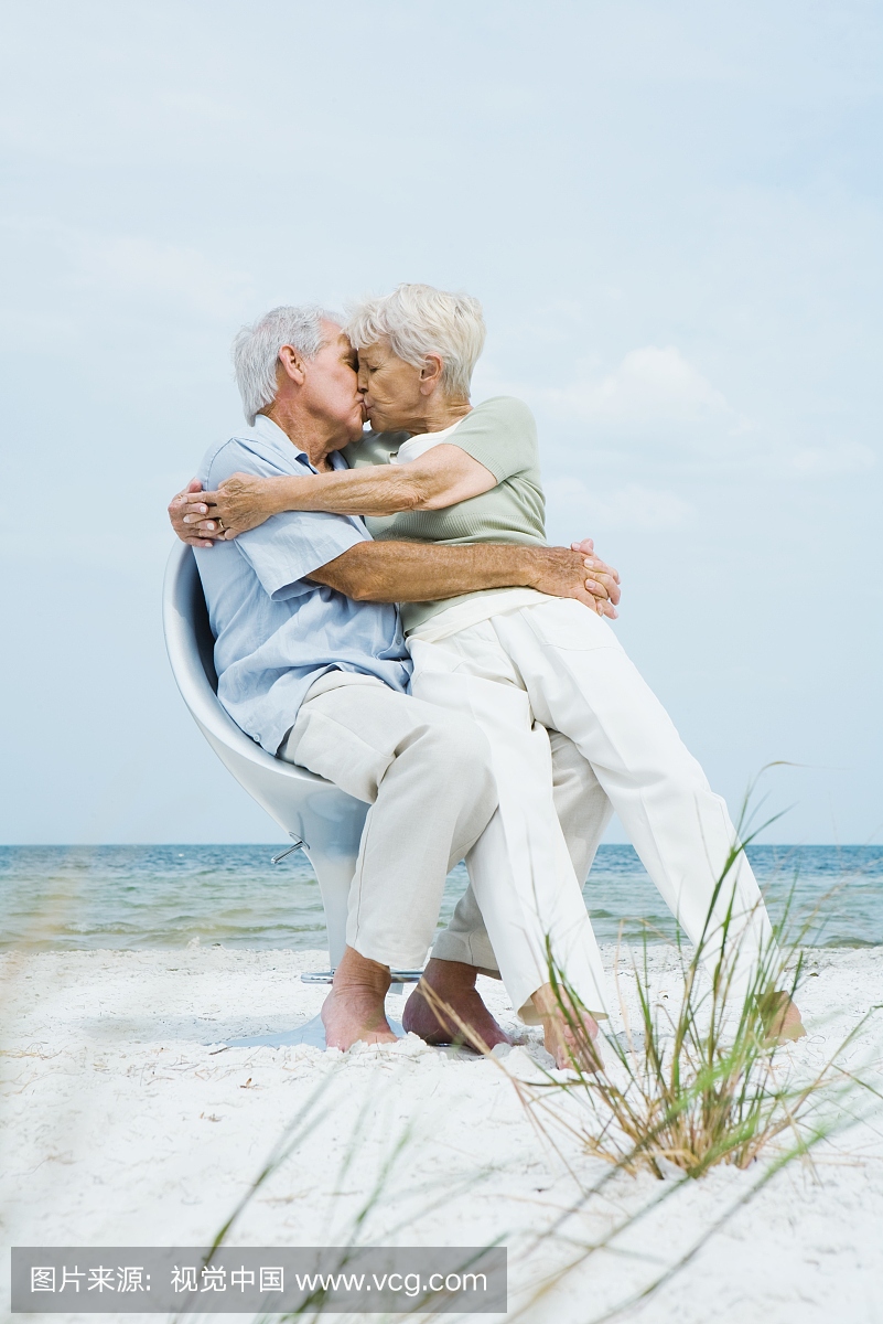 妇坐在椅子上一起在沙滩上,拥抱和亲吻,女人坐