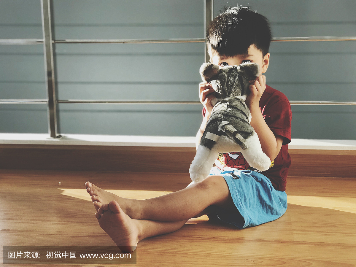 逗人喜爱的男孩在家坐与毛绒的玩具猫