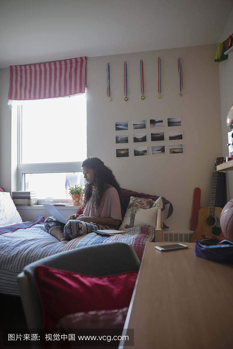 llege student studying at laptop on bed in dorm 