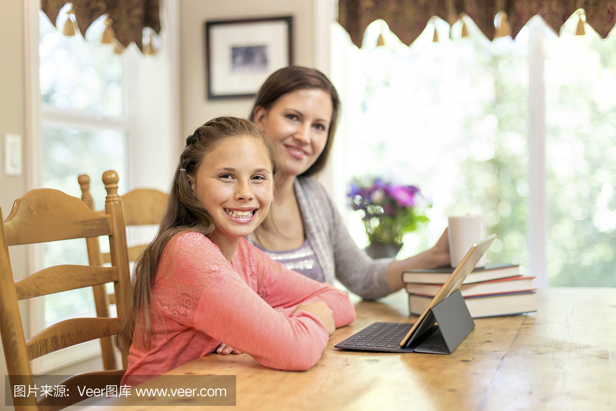 青春期的女孩微笑着使用智能平板电脑做家庭作