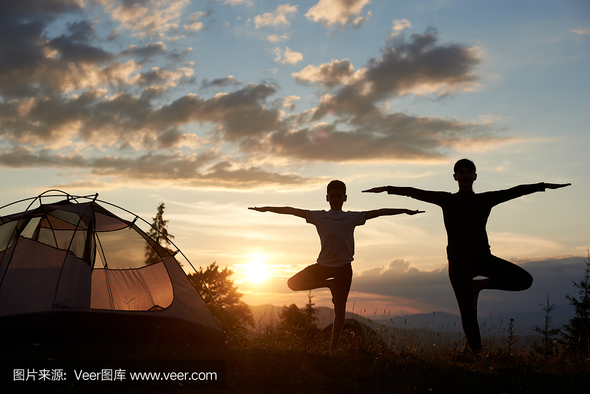 女人和男孩站在瑜伽姿势在美丽的天空下露营附