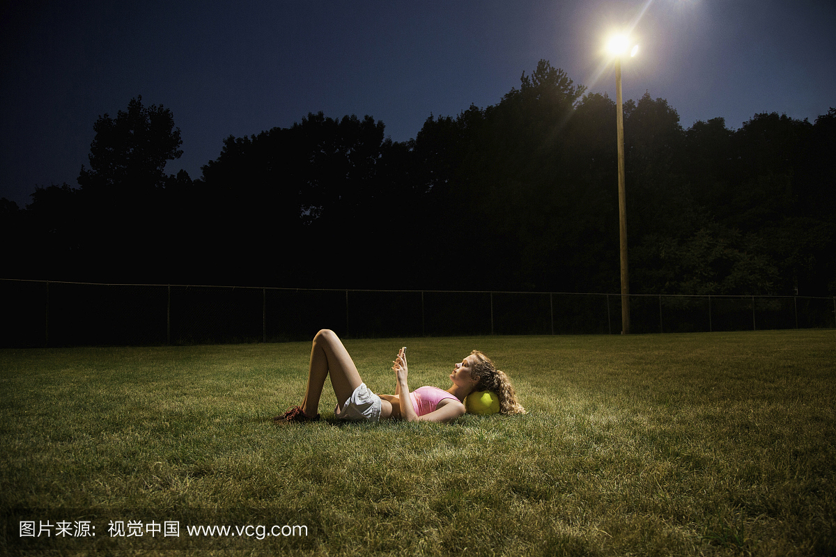 在晚上使用手机躺在足球场上的女孩