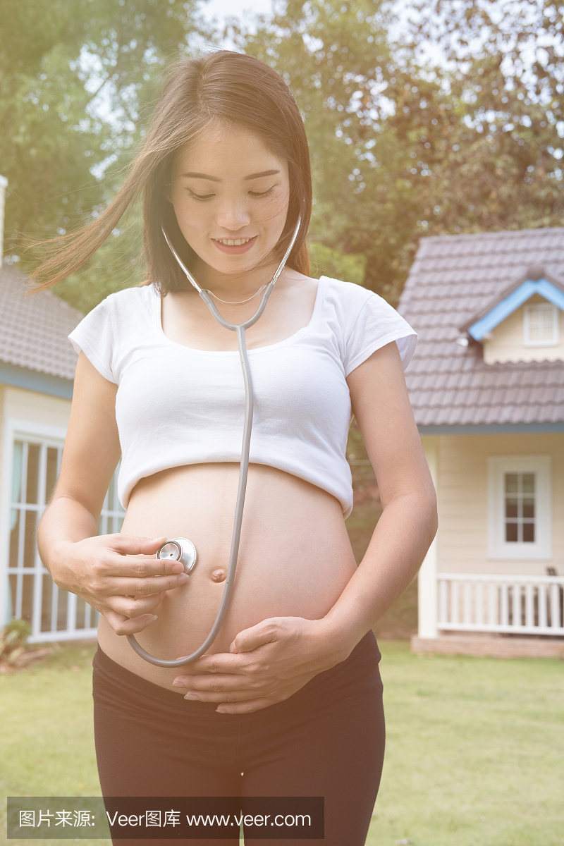 亚裔孕妇使用听诊器听她婴儿的心音,在她家前