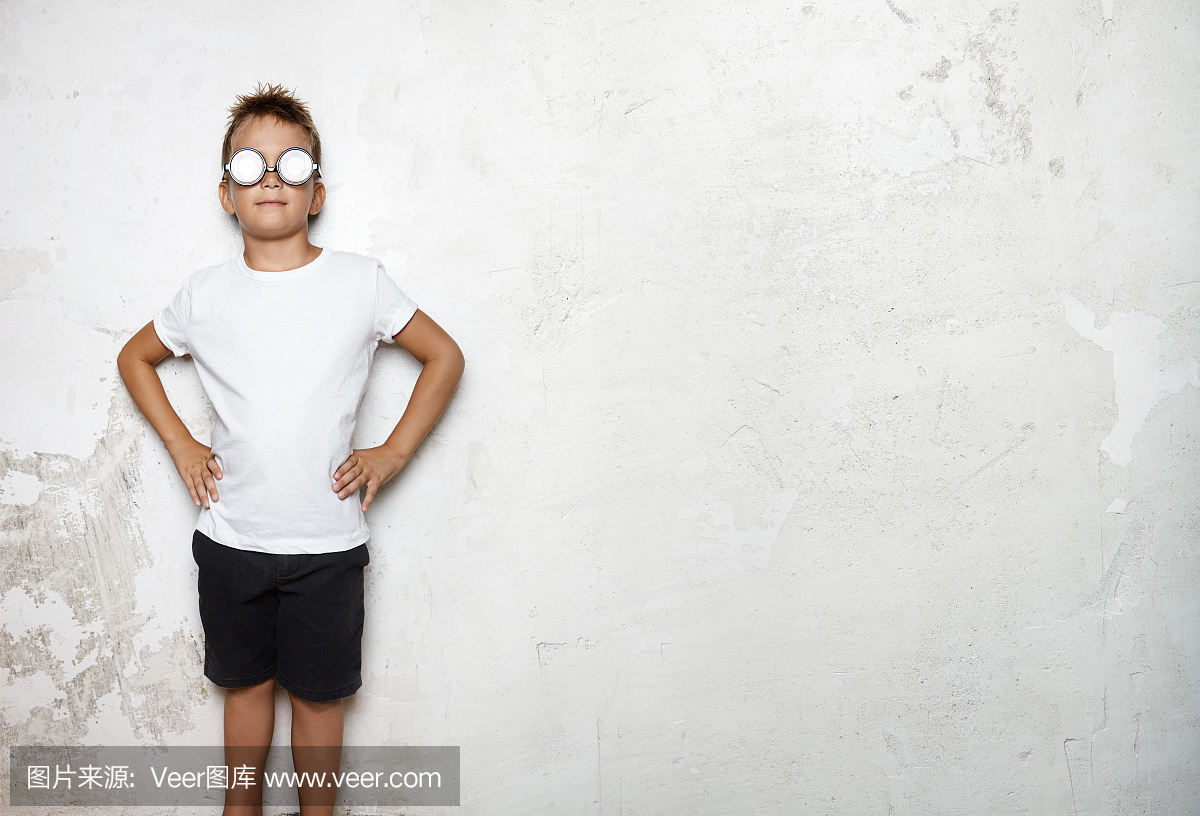 男孩穿着白色t恤,短裤站在墙上的背景