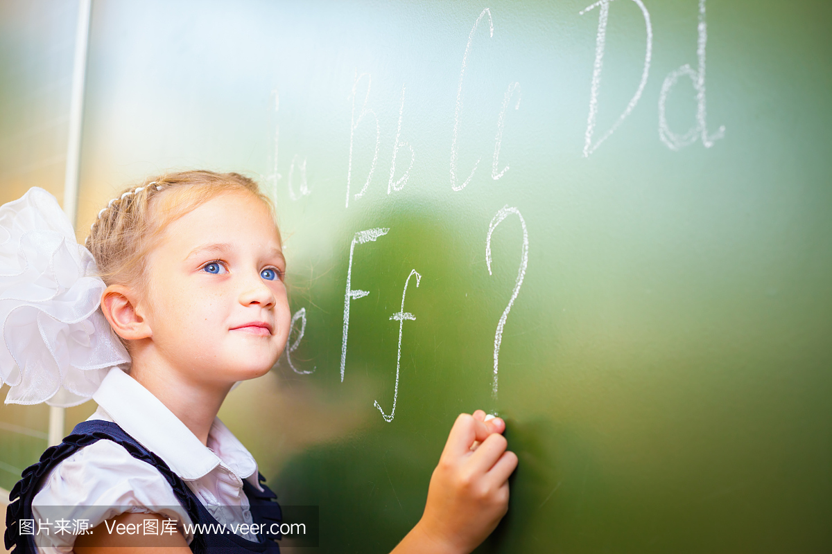 女小学生用黑板上的粉笔写英文字母