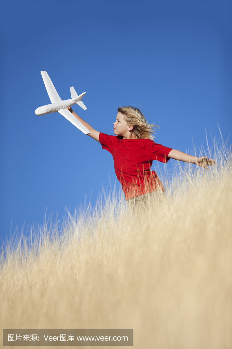 在草地玩玩具滑翔机飞机的年轻男孩