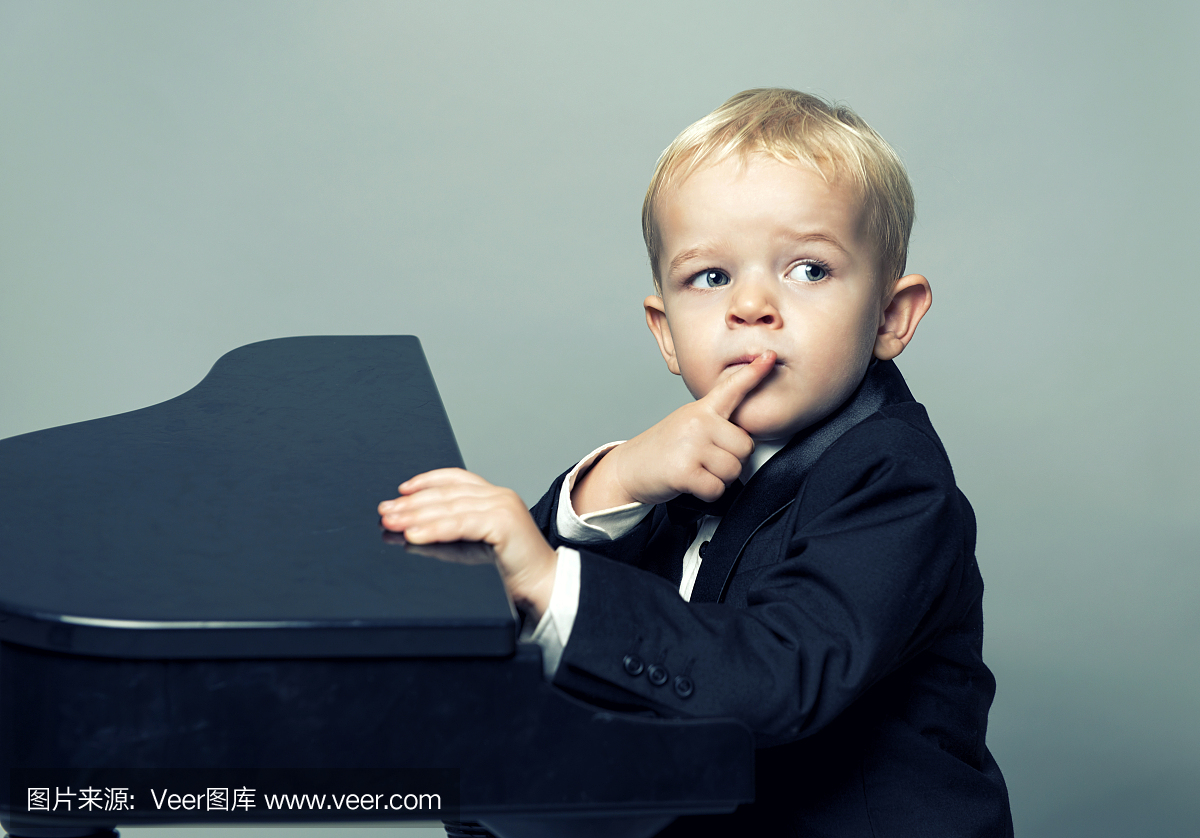 无尾礼服的男孩坐在钢琴的前面