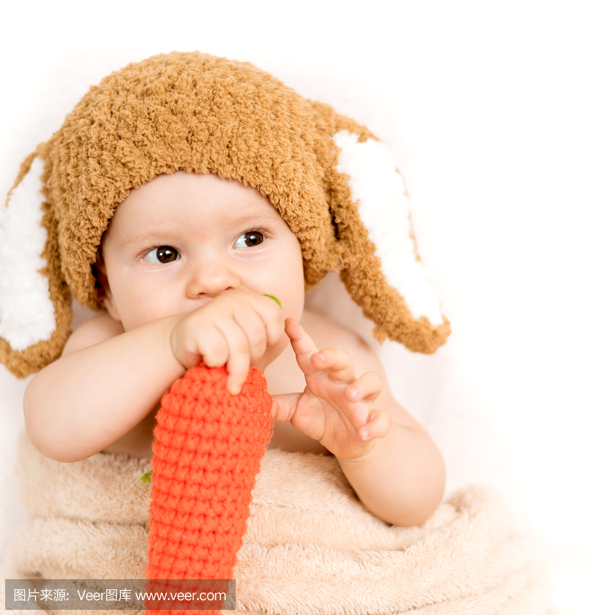 一个可爱的小宝宝戴着兔子帽子吃一个玩具胡萝
