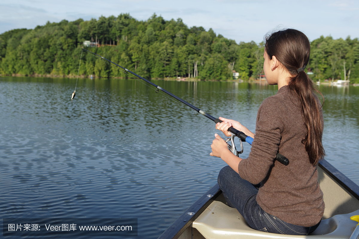 在早晨阳光下从独木舟钓鱼的女孩在湖上