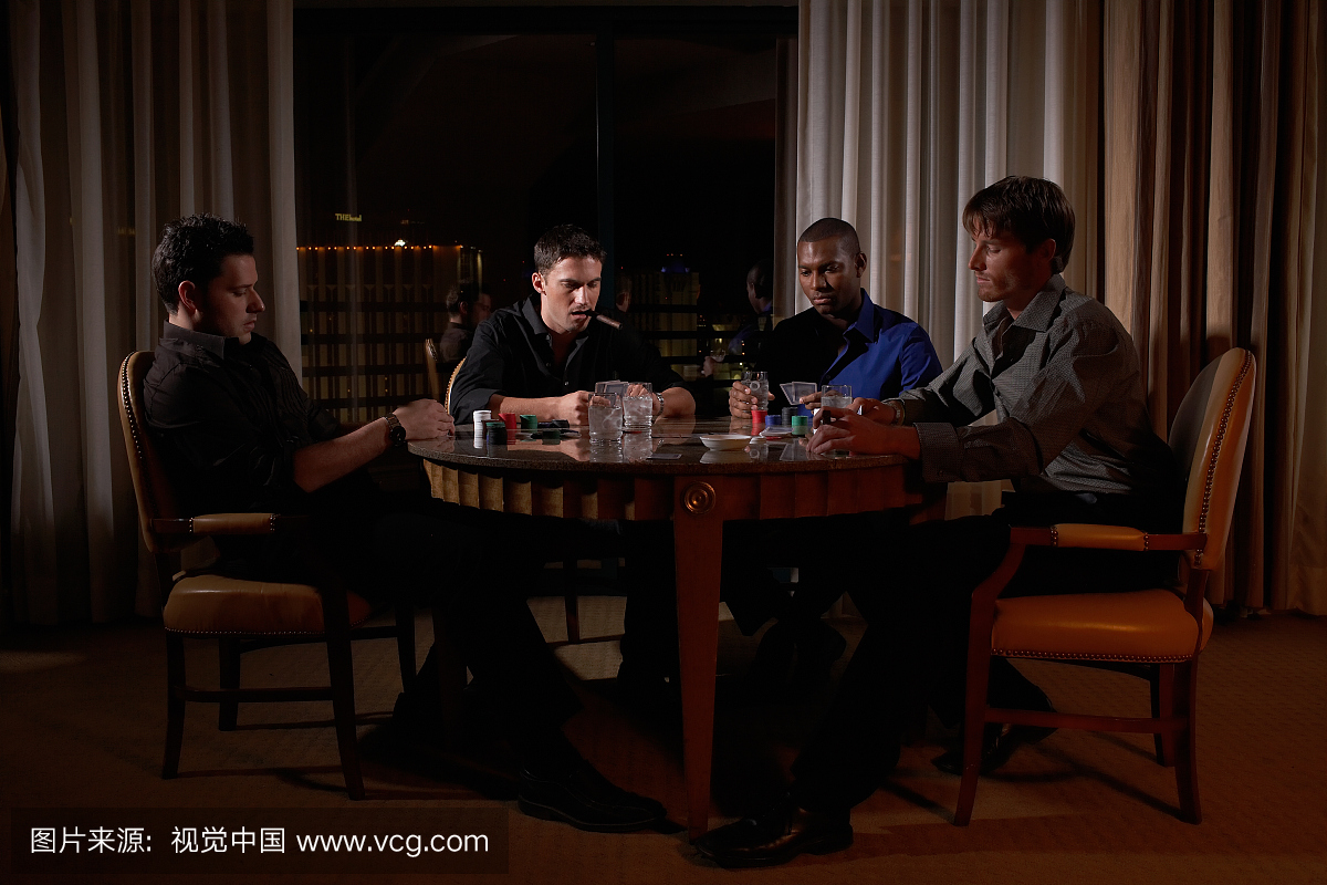 四人坐在圆桌上黑暗的酒店房间玩纸牌,一个吸