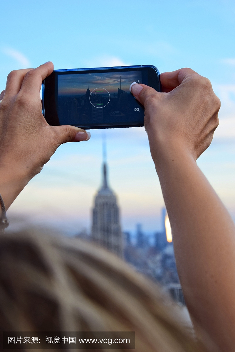 通过智能手机拍摄天空的女人摄影大厦的裁剪图