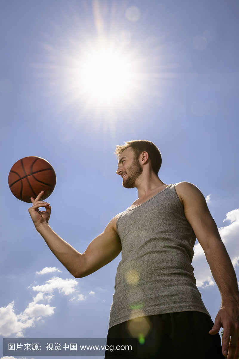 年轻的男性篮球运动员平衡和旋转球在手指