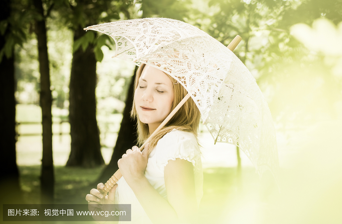 在阳光明媚的一天拿着白色蕾丝遮阳伞的女人