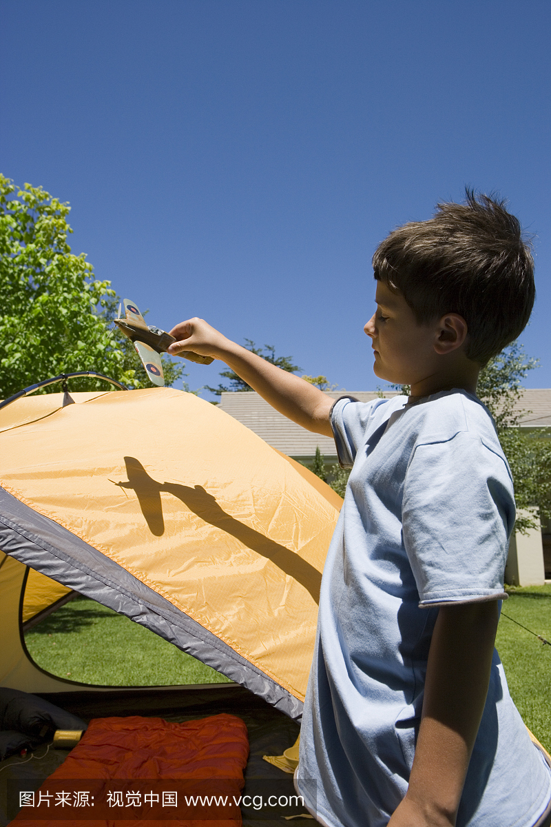 男孩(8-10)玩玩具飞机旁边的圆顶帐篷在花园草