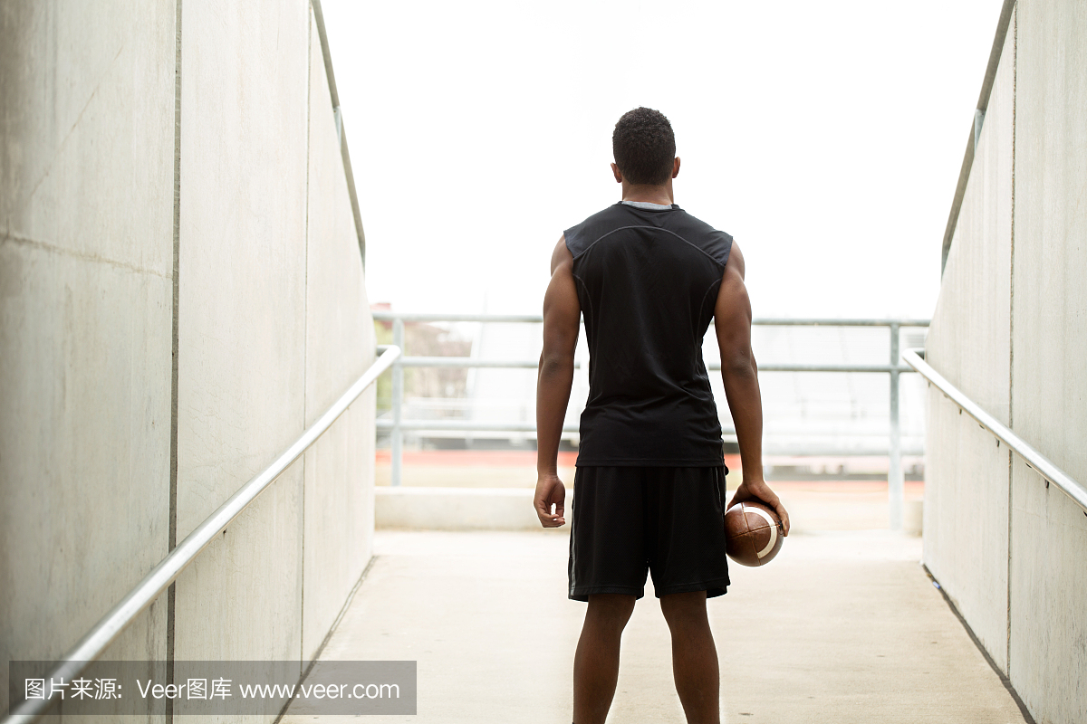 非洲裔美国青少年持有足球的后视图。