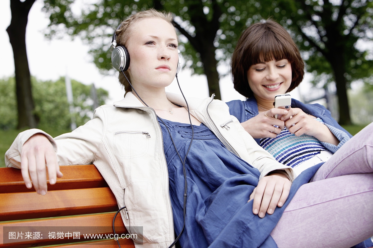 两个女朋友坐在长凳上用MP3播放器和手机
