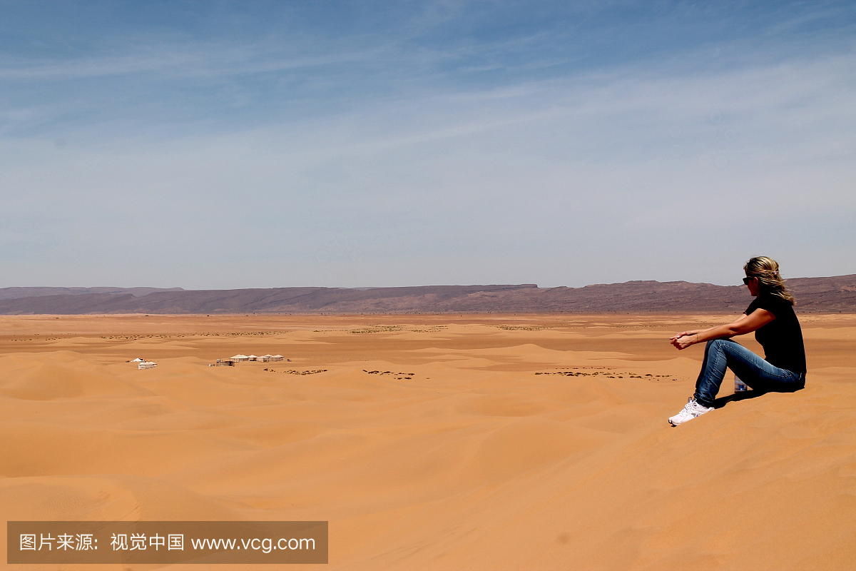 坐在沙丘上的女人的侧视图在撒哈拉沙漠对天空