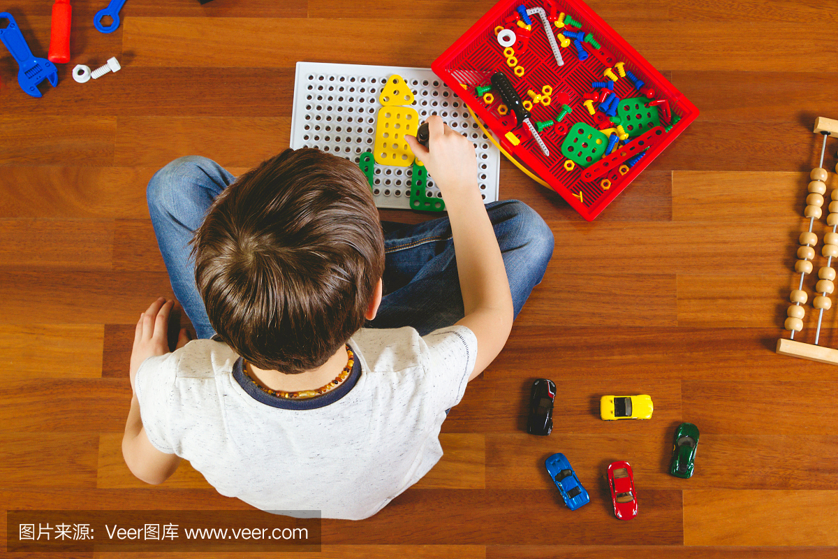 坐在他的房间的地板上的孩子玩玩具工具包。俯