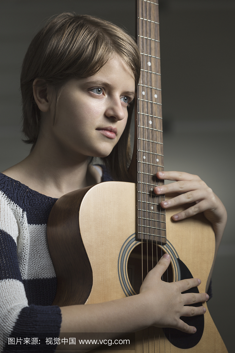 Thoughtful teenager holding guitar against wall