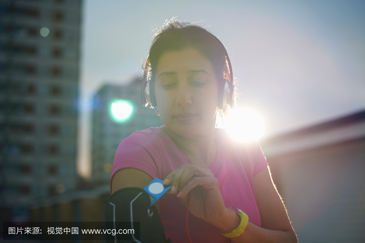 成熟女跑步者在黄昏时从MP3装置中取出MP3