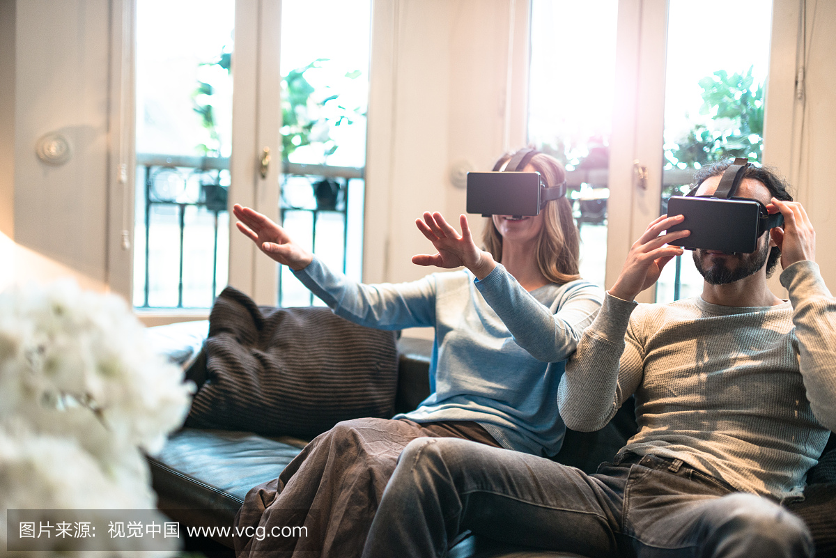 夫妇在家里使用VR模拟器在沙发上